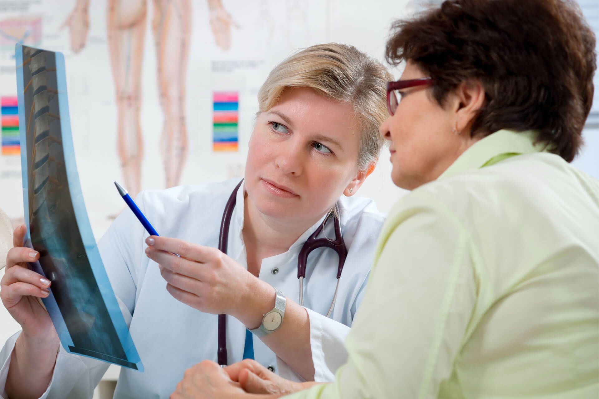 Ärztin erklärt einer Patientin in ihrer Ordination ein Knochenröntgen.