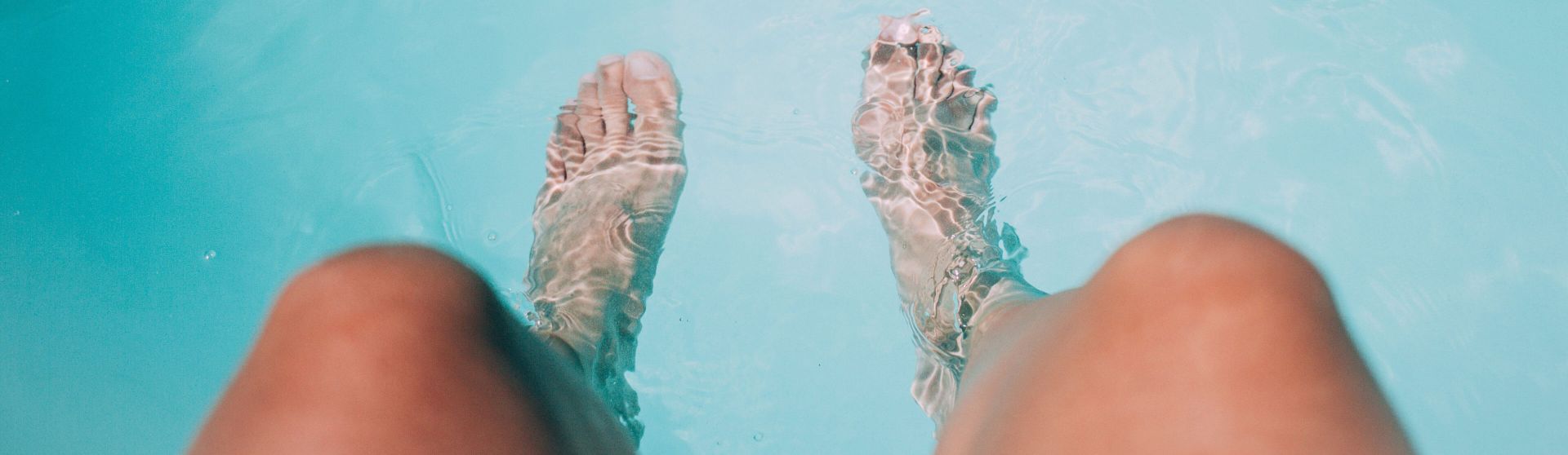 Frau lässt ihre Füße in den Swimmingpool hängen.