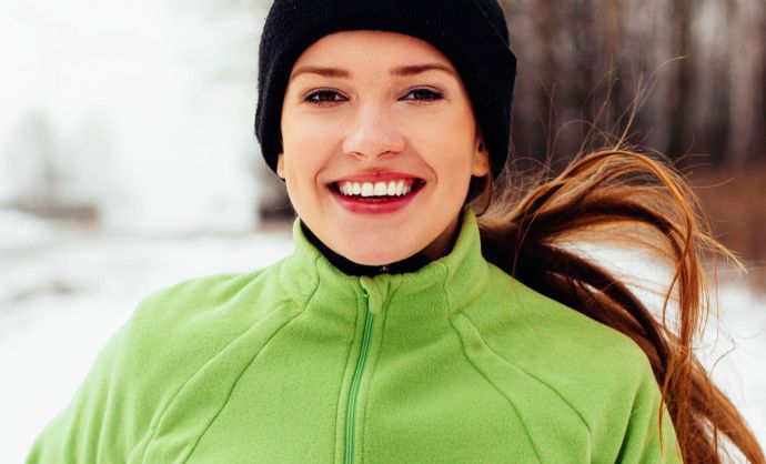 Junge Frau joggt durch eine verschneite Winterlandschaft.