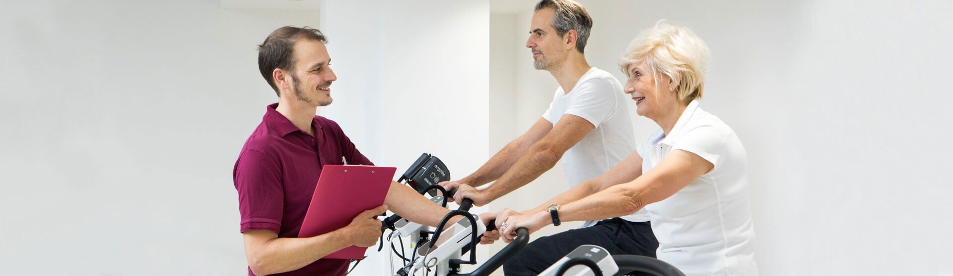 Patienten sitzen am Ergometer, Physiotherapeut überwacht die Übungen.