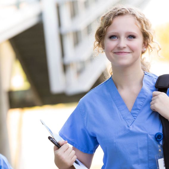Junge Pflegerin geht lächelnd in eine Klinik.