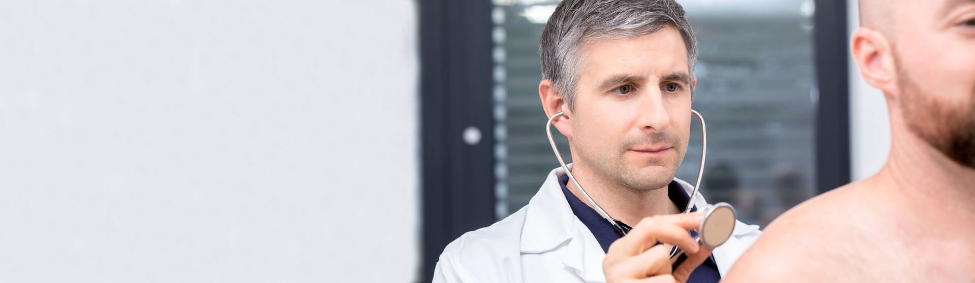 Arzt hört den Rücken eines Patienten mit einem Stethoskop ab.