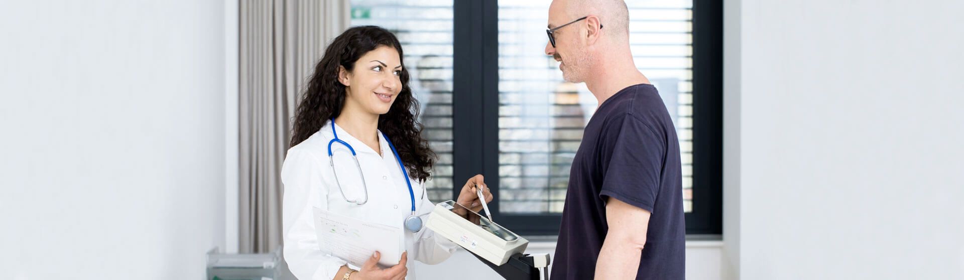 Patient steht auf der Waage, Ärztin liest das Gewicht ab.