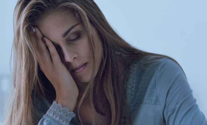 Junge Frau sitzt im Bett und hält den schmerzenden Kopf.