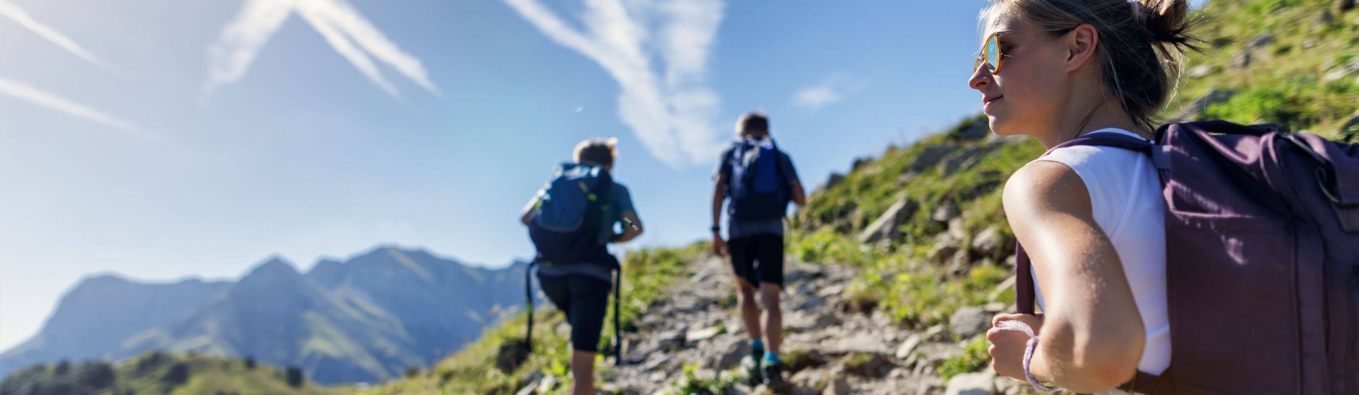 Drei junge Menschen gehen bei Sonnenschein auf einen Berg.