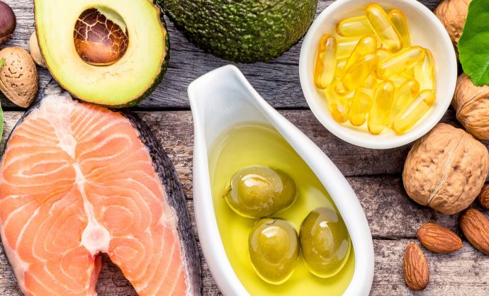 Gesunde Lebensmittel wie Lachs, Avocado, grüne Oliven und Nüsse auf einem Holzbrett.