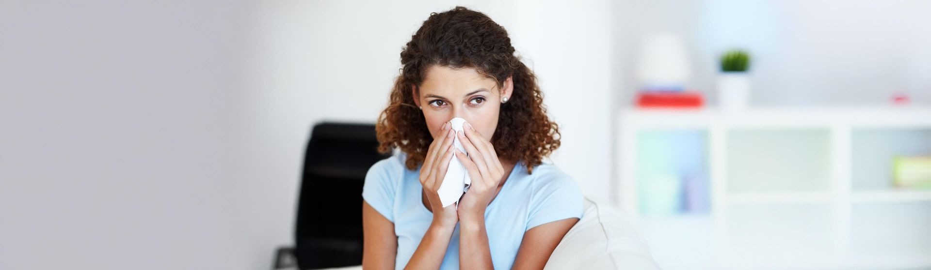 Eine Frau sitzt auf einem Sessel und schnäuzt sich die Nase.