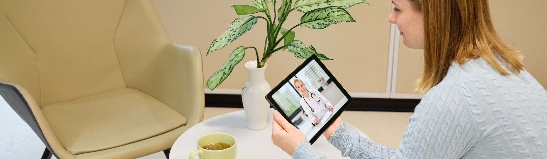 Patientin sitzt am Tisch mit Tablet, Ärztin führt Telekonsultation durch.