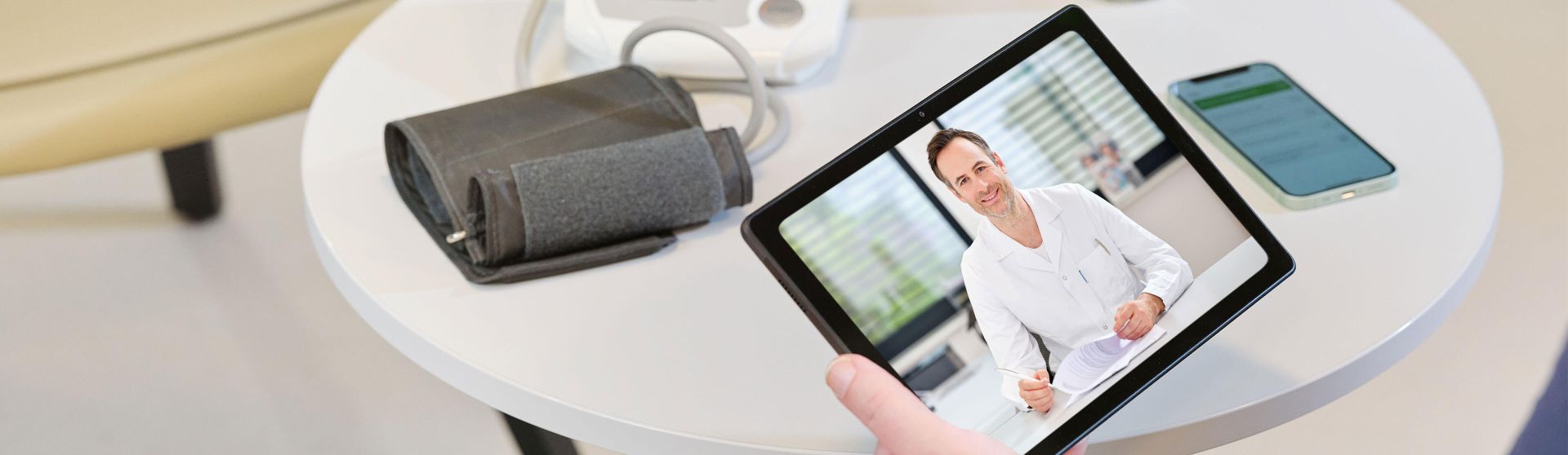 Blutdruckmessgerät, Handy und Tablet mit Telekonsultation am Tisch.