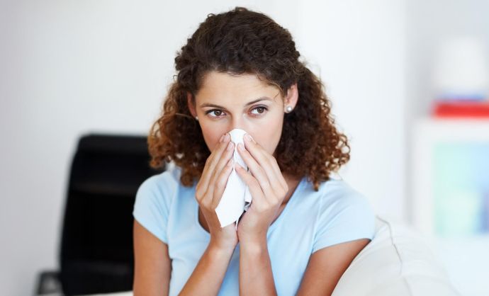 Eine Frau sitzt auf einem Sessel und schnäuzt sich die Nase.