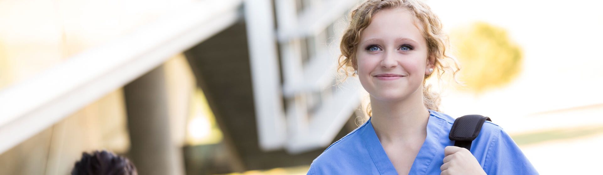 Junge Pflegerin geht lächelnd in eine Klinik.