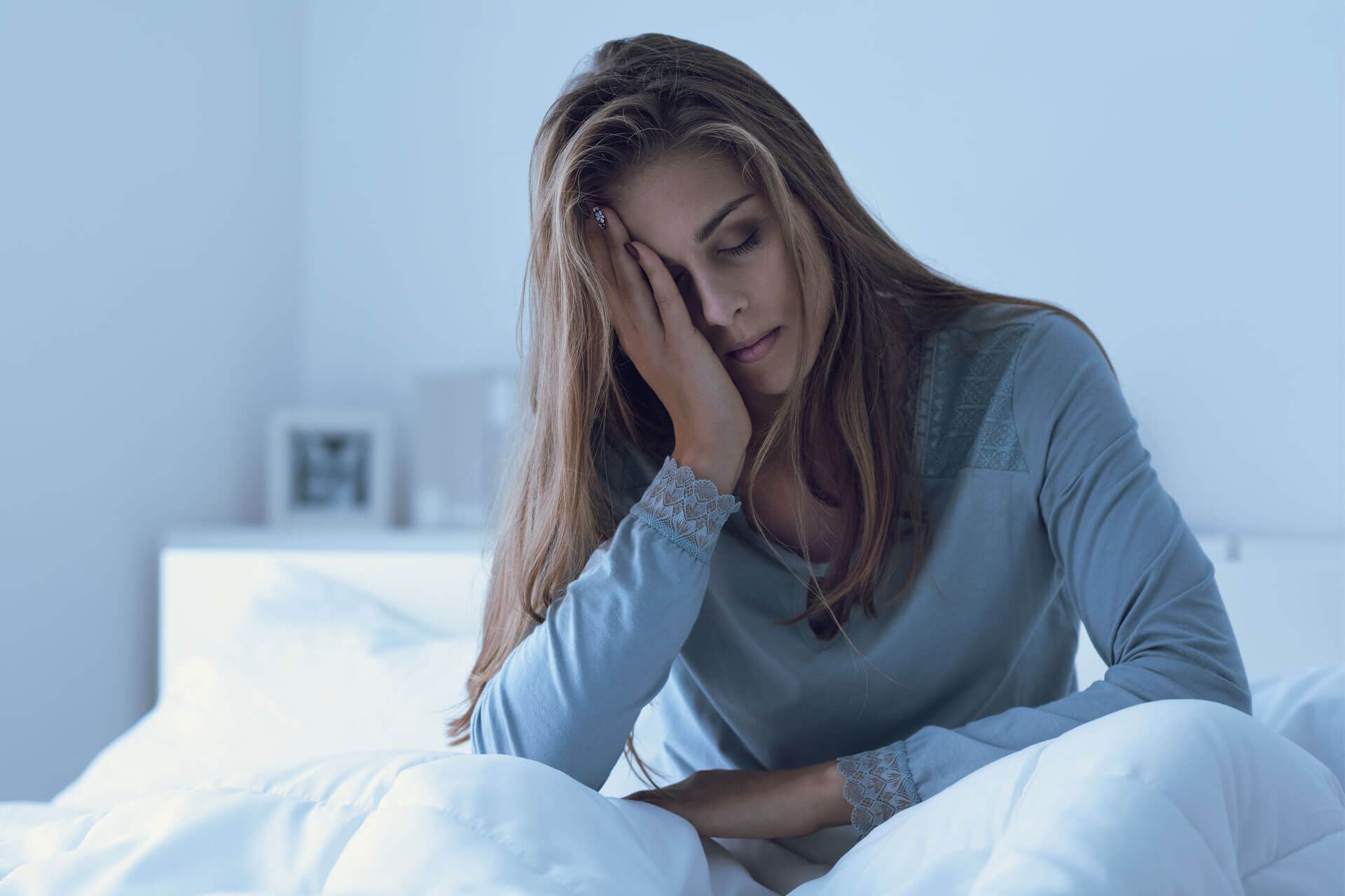 Junge Frau sitzt im Bett und hält den schmerzenden Kopf.