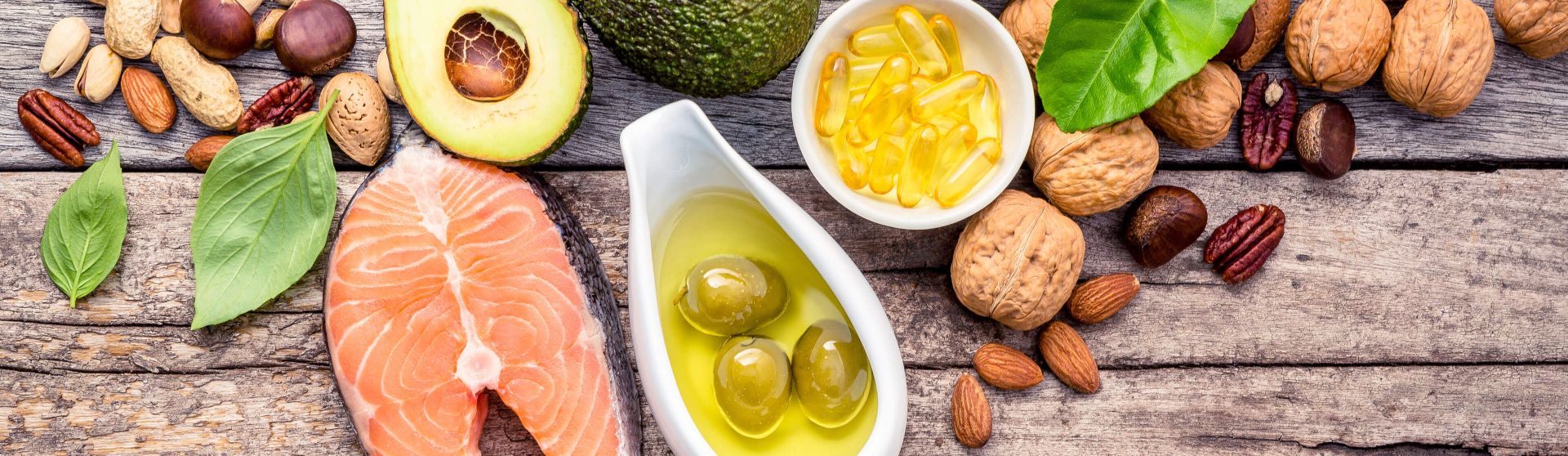 Gesunde Lebensmittel wie Lachs, Avocado, grüne Oliven und Nüsse auf einem Holzbrett.