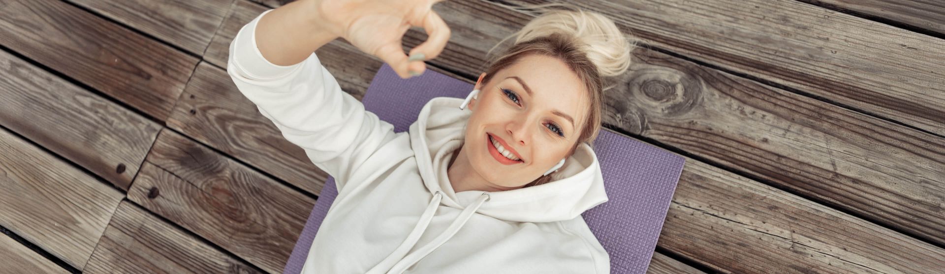 Junge Frau liegt auf einer Sportmatte und gibt lächelnd ein OK-Zeichen.