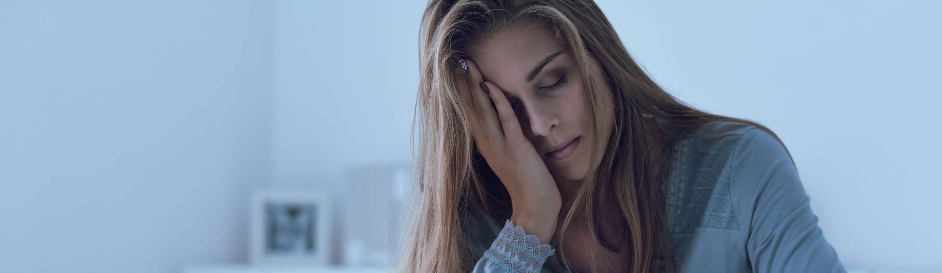 Junge Frau sitzt im Bett und hält den schmerzenden Kopf.