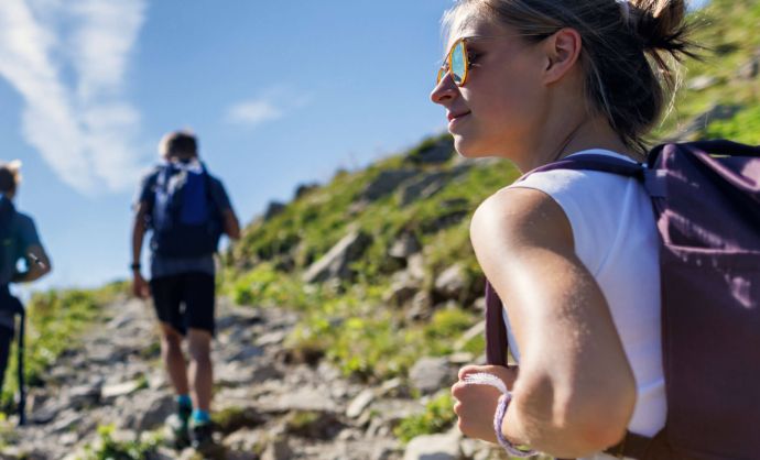 Drei junge Menschen gehen bei Sonnenschein auf einen Berg.