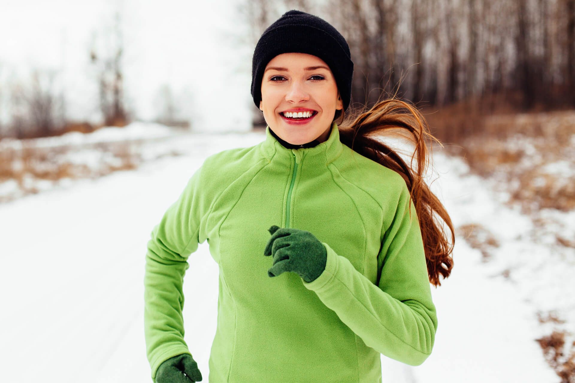 Junge Frau joggt durch eine verschneite Winterlandschaft.