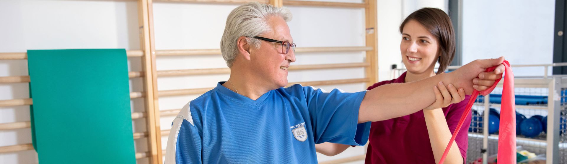 Physiotherapeutin unterstützt einen Patienten bei Theraband-Übungen.