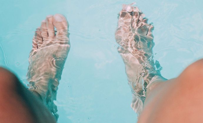 Frau lässt ihre Füße in den Swimmingpool hängen.