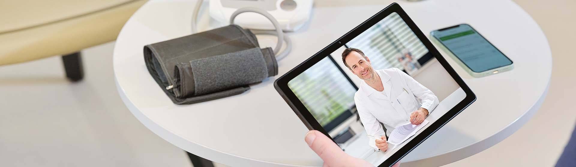 Blutdruckmessgerät, Handy und Tablet mit Telekonsultation am Tisch.