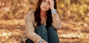 Junge Frau sitzt im Park und hält den schmerzenden Kopf.