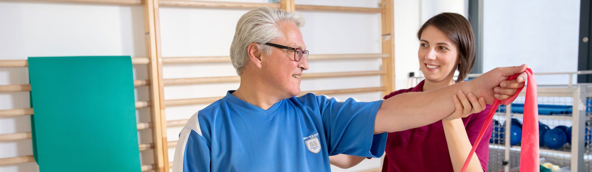 Physiotherapeutin unterstützt einen Patienten bei Theraband-Übungen.