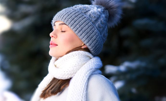 Frau steht im Freien und atmet kalte Winterluft ein.