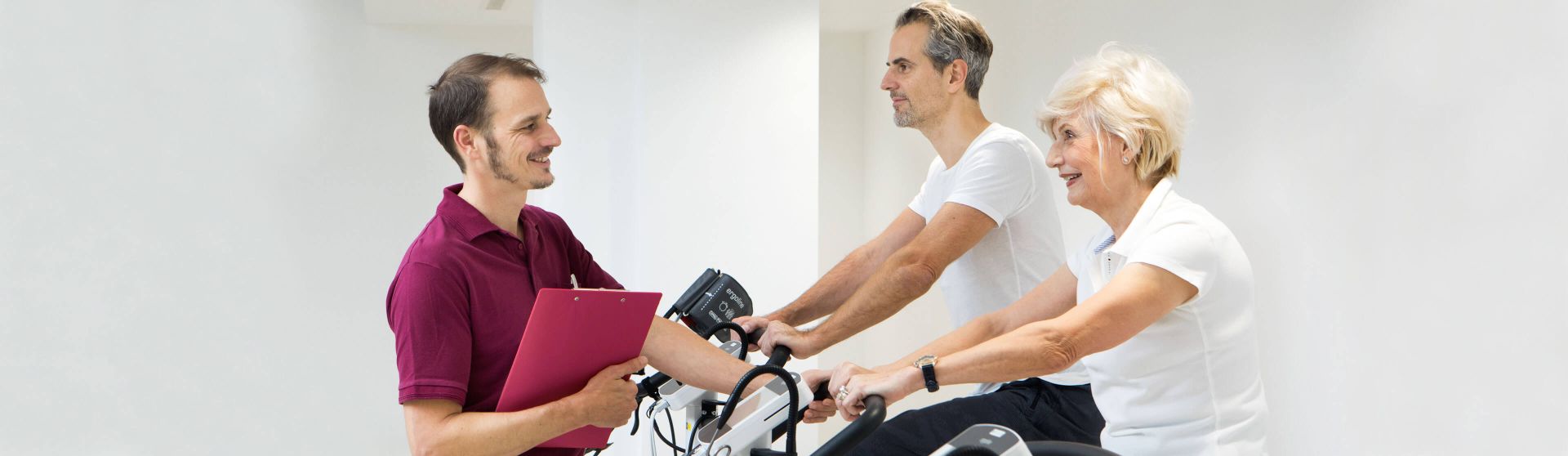 Patienten sitzen am Ergometer, Physiotherapeut überwacht die Übungen.