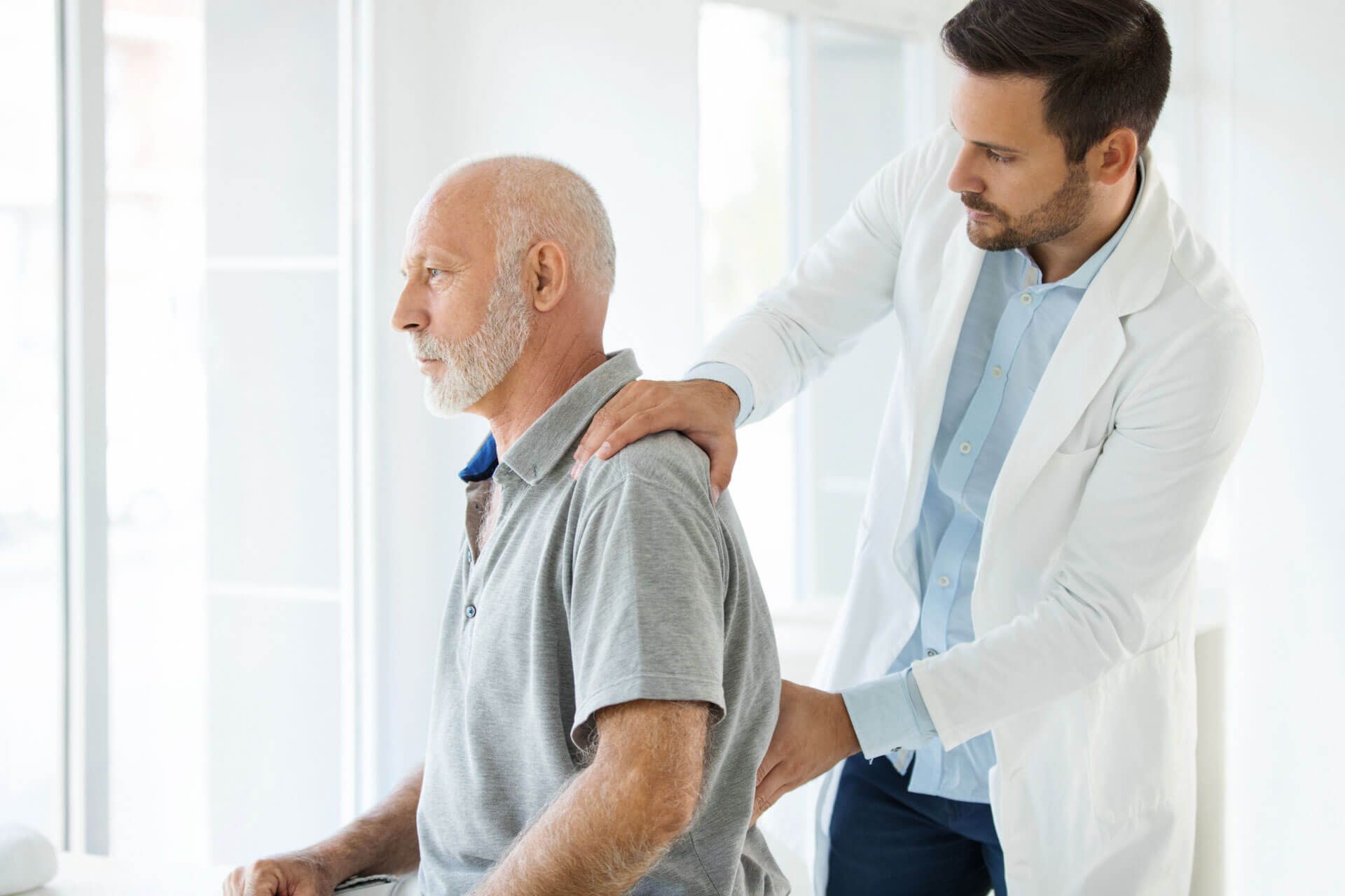 Arzt ertastet bei Patient Schmerzen im unteren Rücken.
