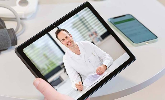 Blutdruckmessgerät, Handy und Tablet mit Telekonsultation am Tisch.