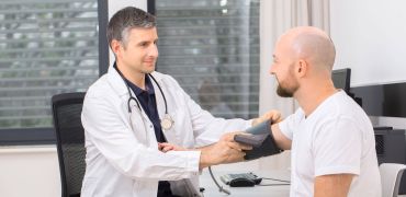 Arzt misst bei männlichem Patient den Blutdruck.